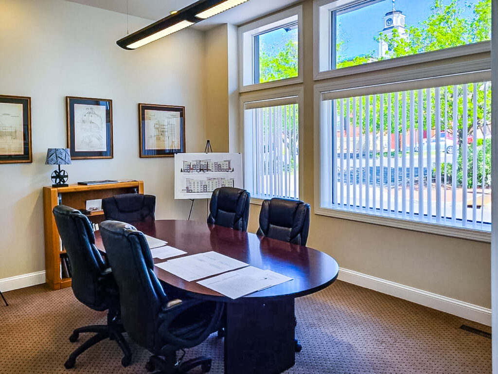 Inside the DFC-LMA offices. This is the meeting room with a large oval table, 5 black leather office chairs, and a picture window that shows a summer view of the downtown Winchester VA walking mall.
