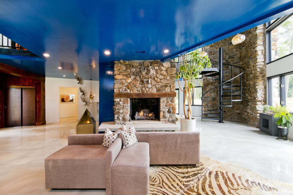 Stylish open concept room with a lustrous blue ceiling, low slung modern sofa, and stone fireplace